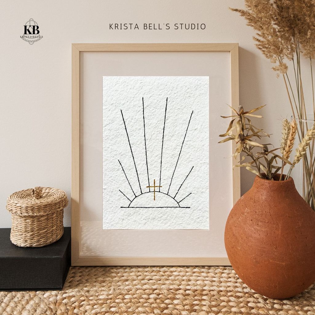 Framed artwork of sunrays and a golden cross, on a neutral wall, featuring 'Krista Bell's Studio' branding.