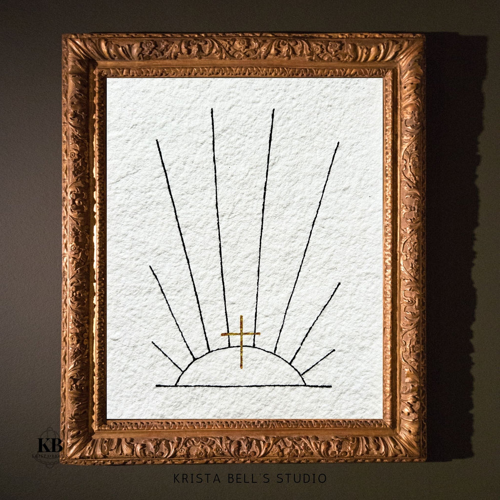 Framed artwork of a sun with a cross on textured paper, branded 'Krista Bell's Studio'.