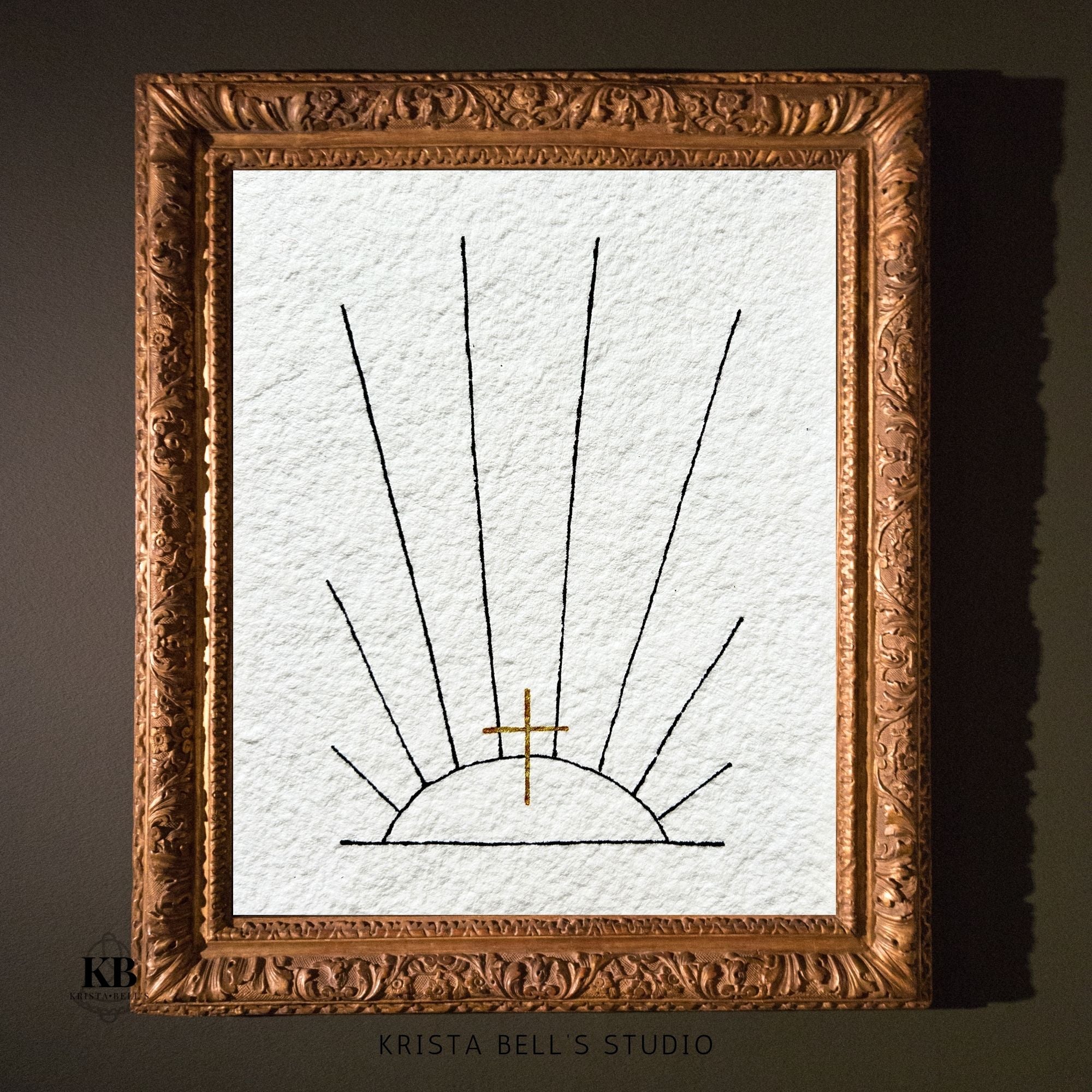 Framed artwork of a sun with a cross on textured paper, branded 'Krista Bell's Studio'.