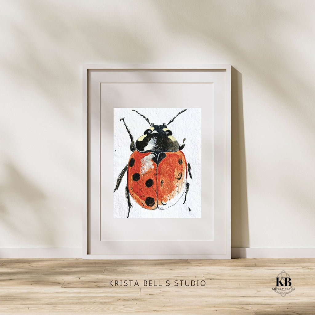 Framed artwork of a ladybug on a light wooden surface with a neutral wall background.