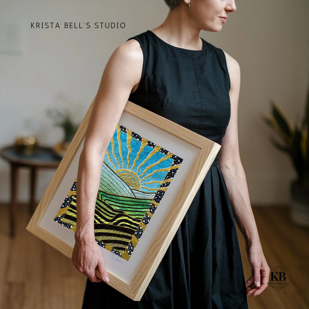 Person holding a framed artwork with a colorful design, standing indoors.