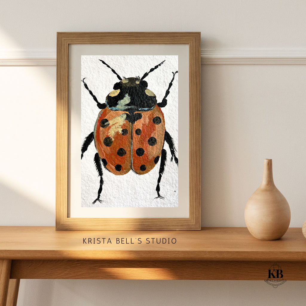 Framed artwork of a ladybug by Krista Bell's Studio on a wooden surface.