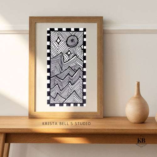 Framed black and white patterned artwork on a wooden shelf with 'Krista Bell's Studio' branding. Black and white modern abstract line art patterned of jagged mountains in the moon light and stars.