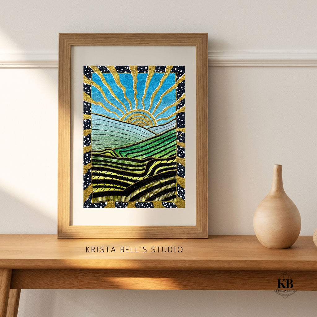 Framed artwork by Krista Bell's Studio on a wooden shelf with a vase.
