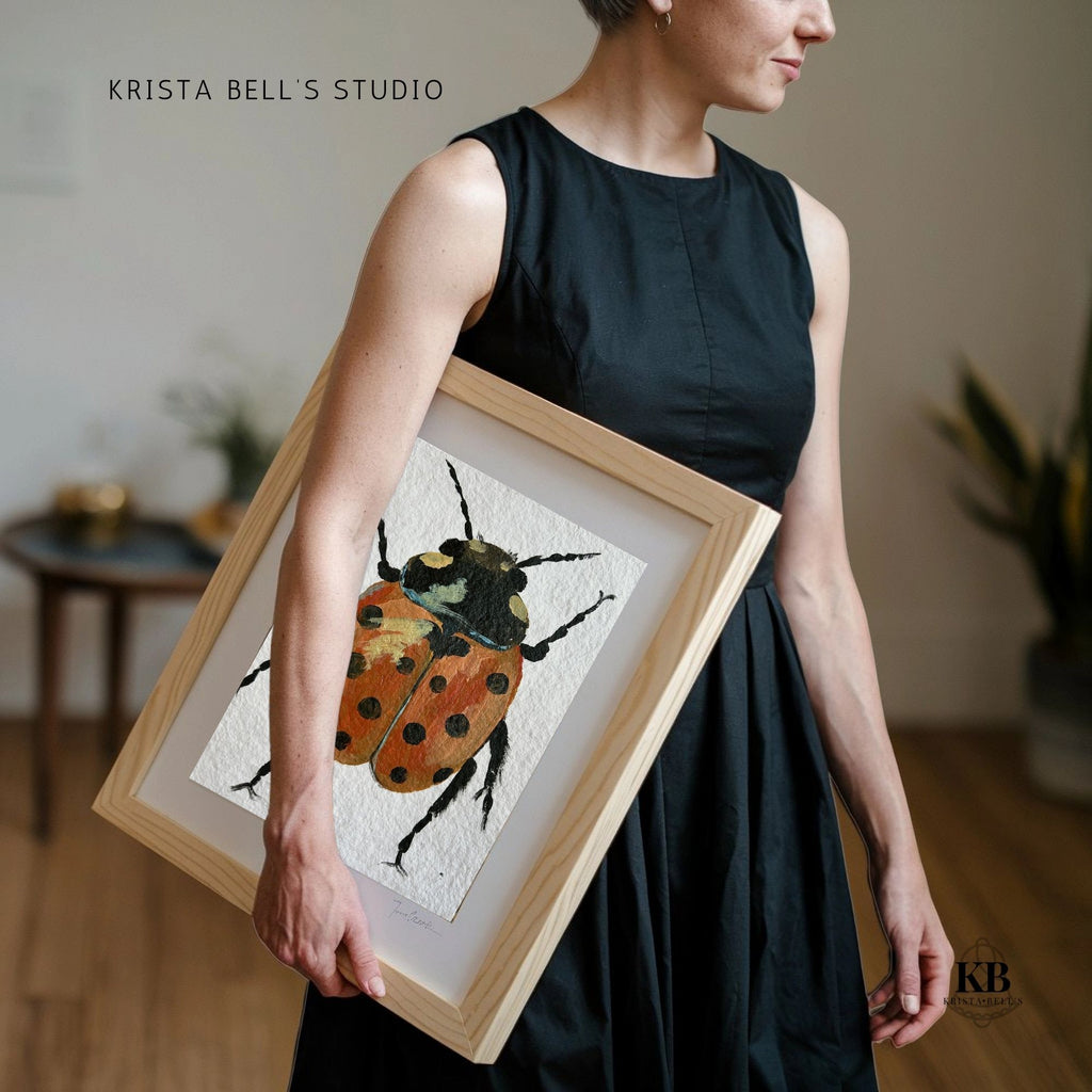 Person holding a framed artwork of a beetle by Krista Bell's Studio