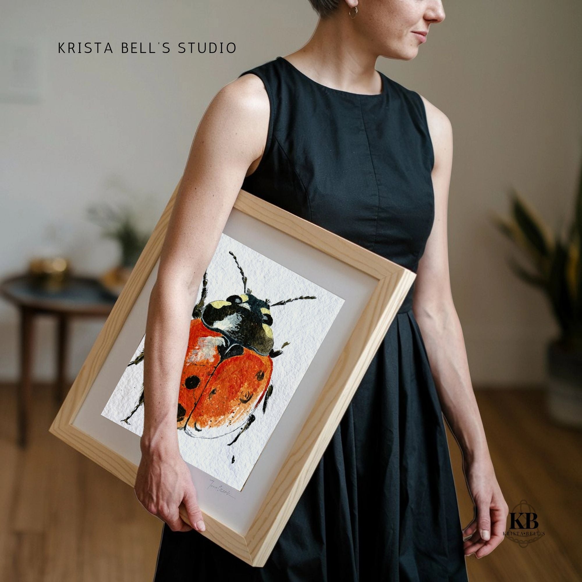 Person holding a framed artwork of a red insect by Krista Bell's Studio