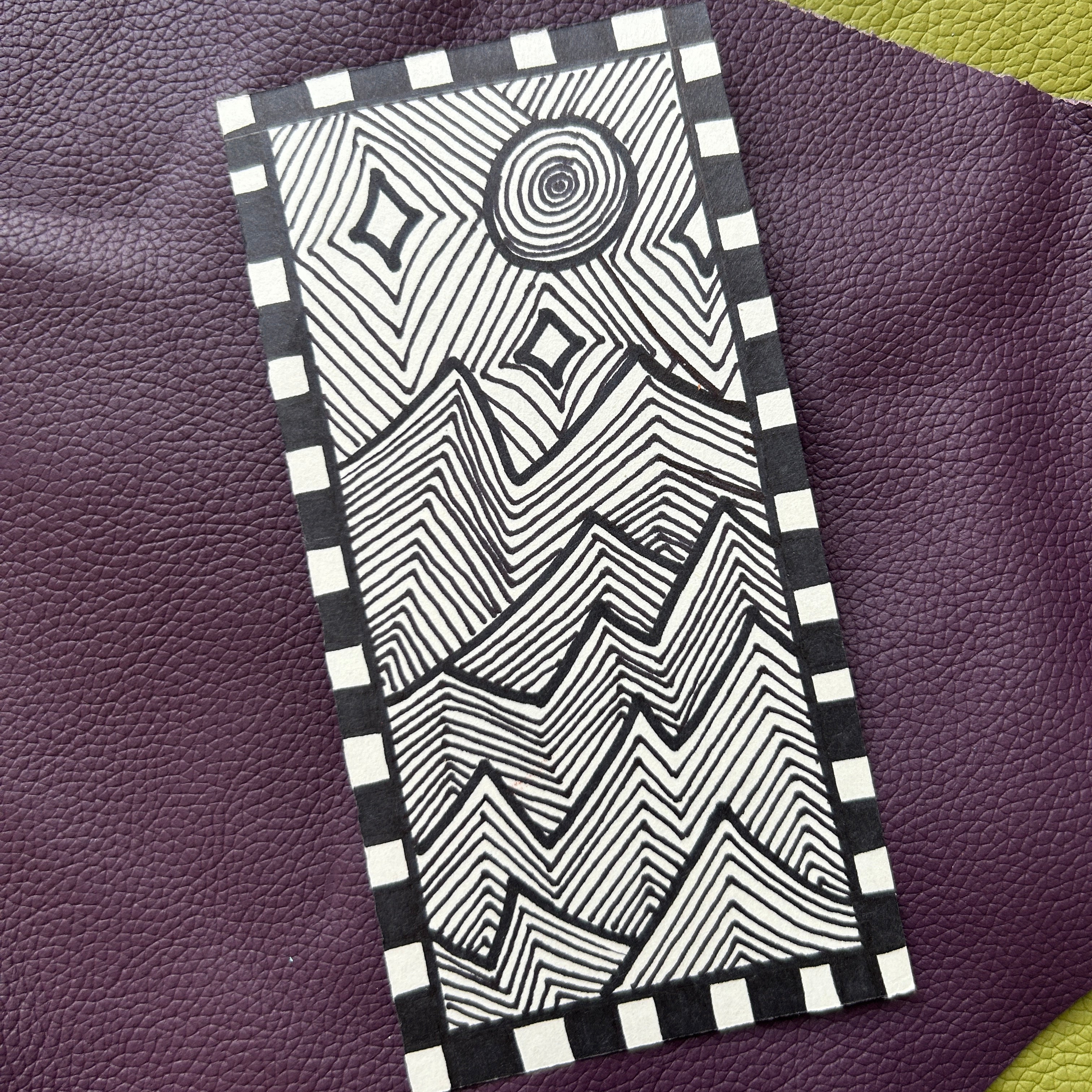 Black and white modern geometric landscape ink drawing with a checker patterned border laying on a textured purple surface.