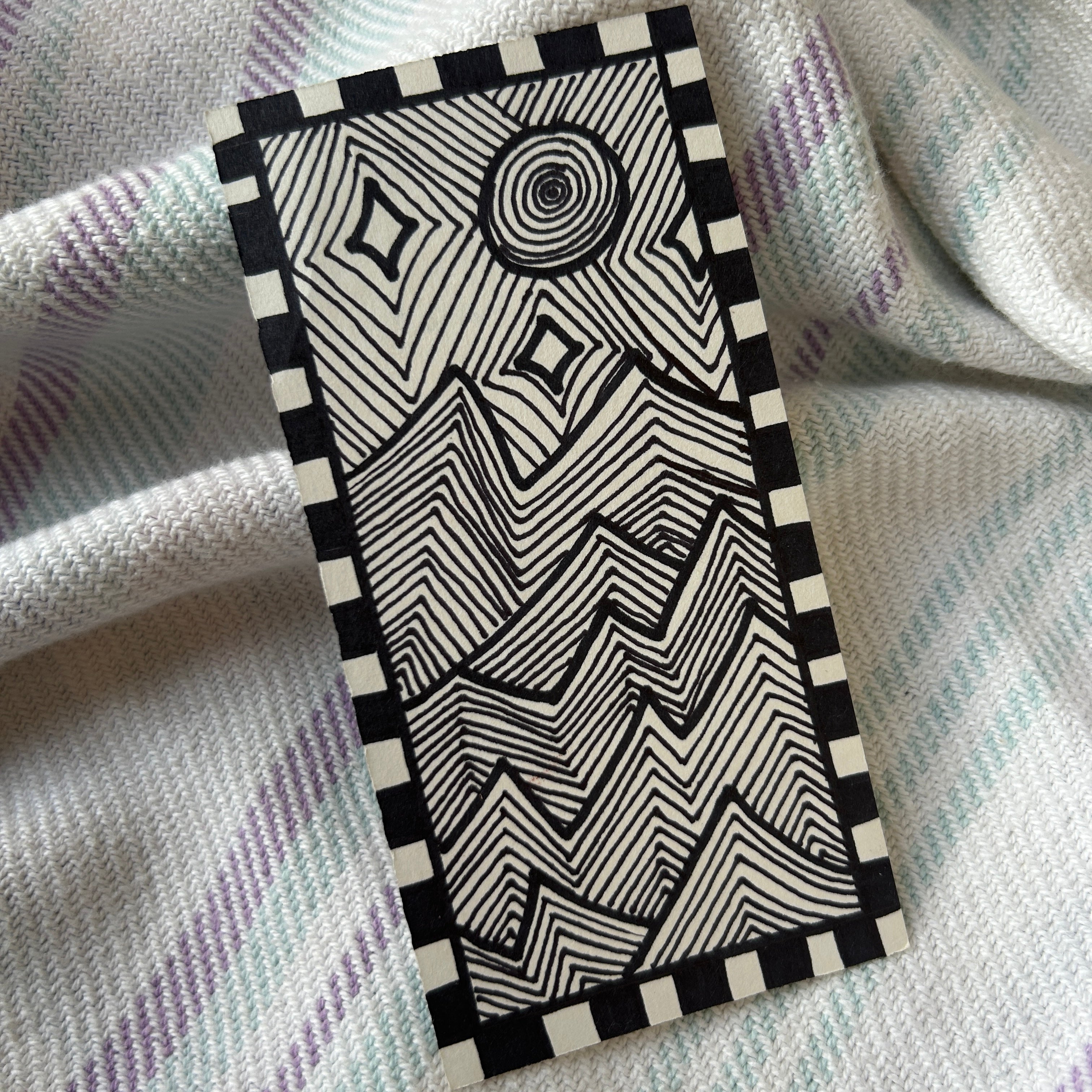 Black and white geometric patterned box bordering a geometric line landscape of jagged mountains and moon light, on a textured fabric background