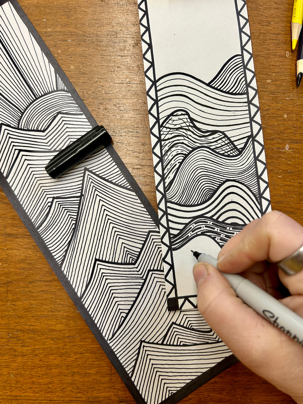 Person drawing a black and white line art design on a piece of paper with a pen.