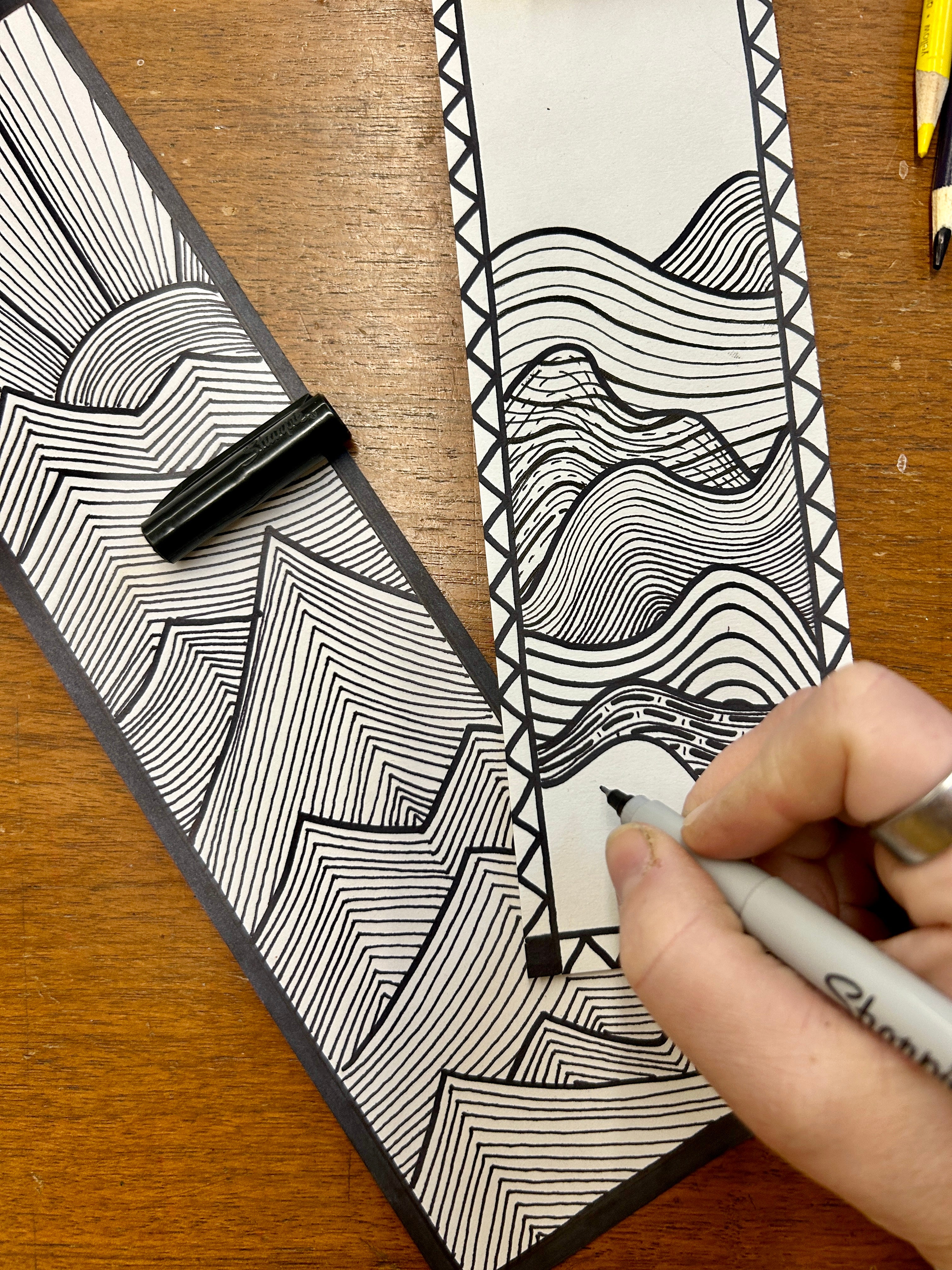 Person drawing a black and white line art design on a piece of paper with a pen.