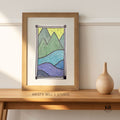 Framed artwork of mountains on a wooden shelf with 'Krista Bell's Studio' branding.