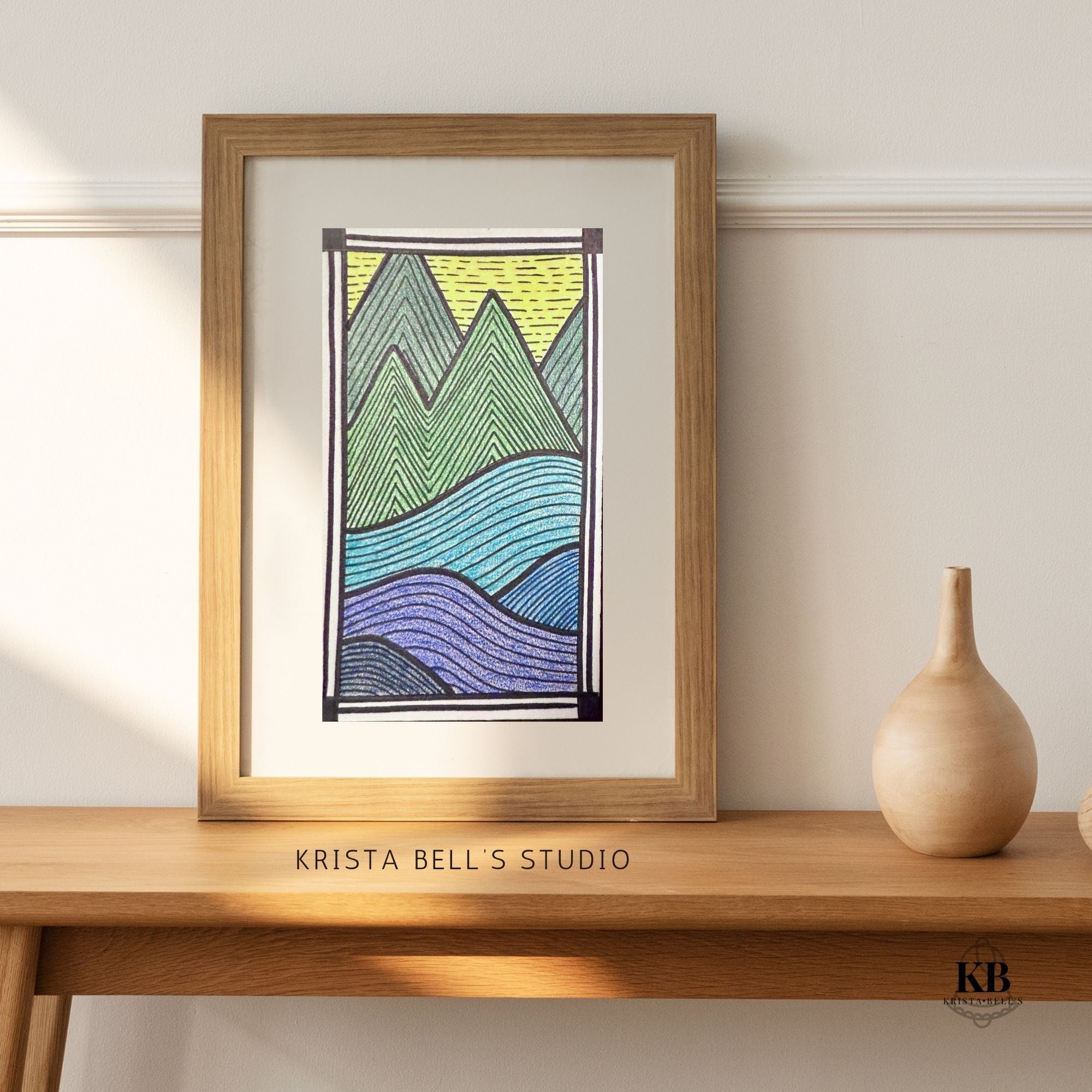Framed artwork of mountains on a wooden shelf with 'Krista Bell's Studio' branding.