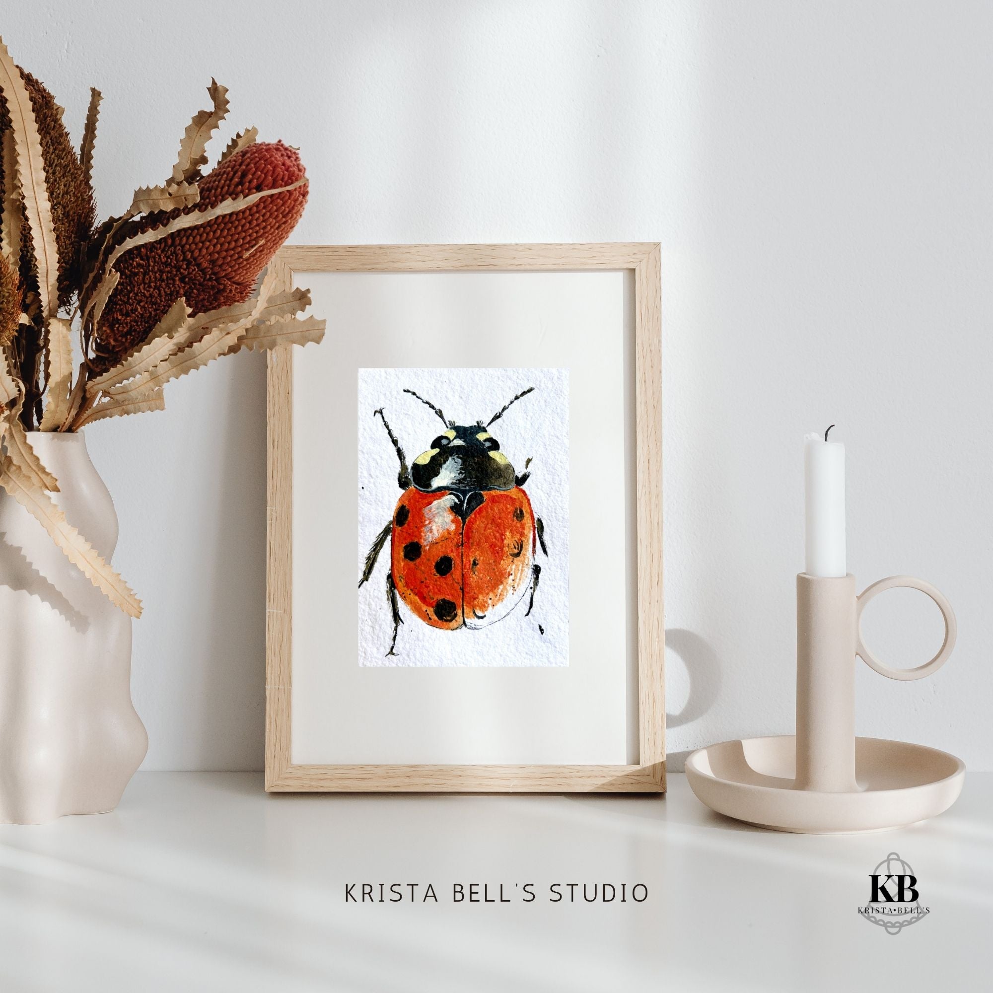 Framed artwork of a ladybug on a white surface with decorative items.