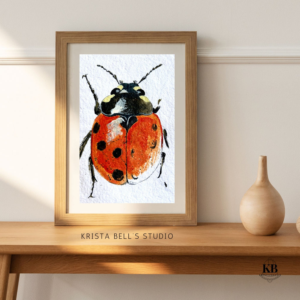 Framed artwork of a ladybug by Krista Bell's Studio on a wooden surface.