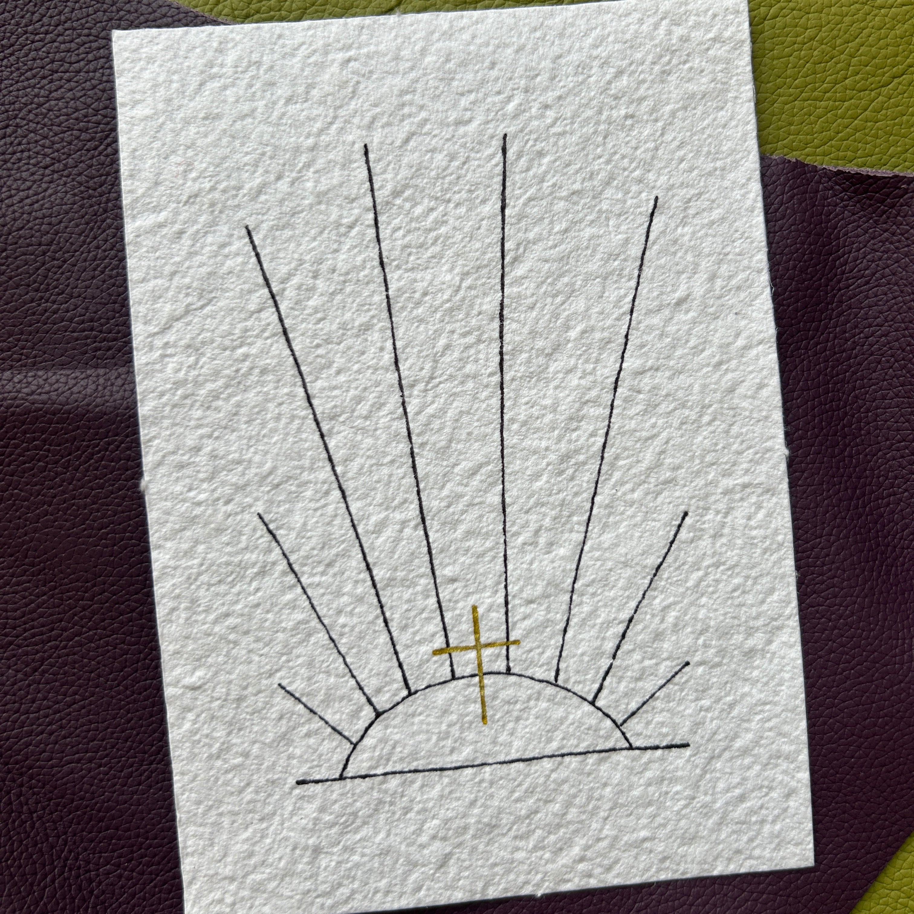 Hand-drawn cross with sunburst pattern on textured paper against a dark background
