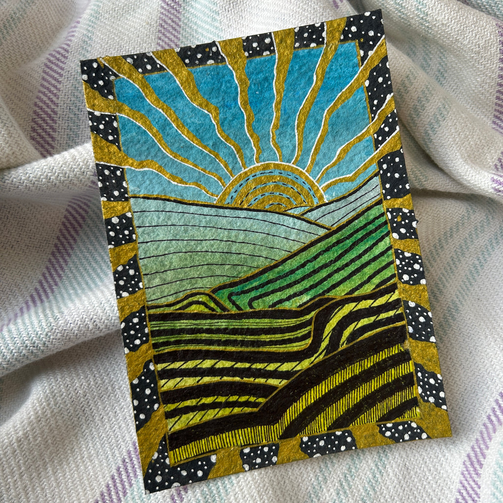 Decorative card with a sun and landscape design on a textured fabric background