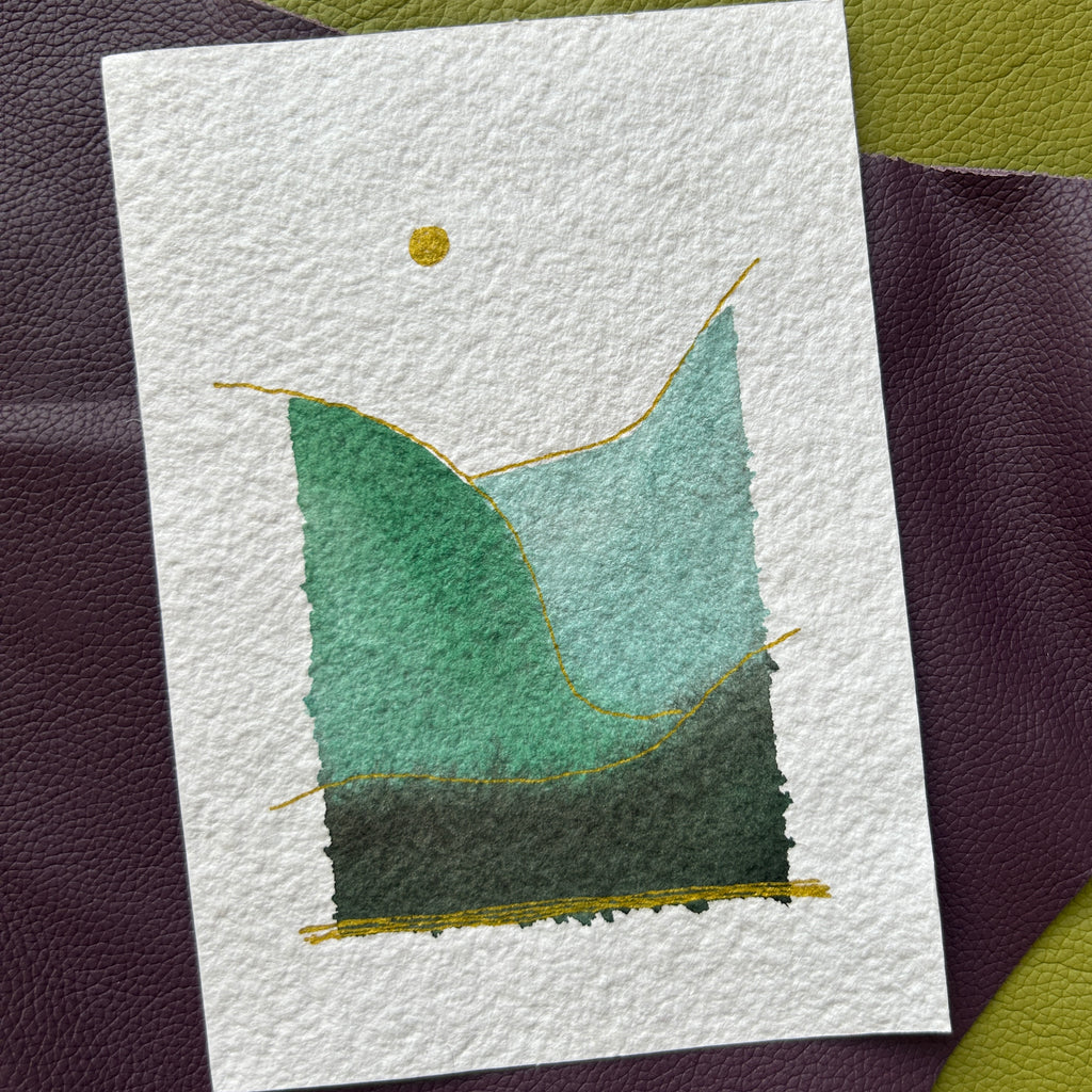 Handmade watercolor landscape card laying on a green purple background.