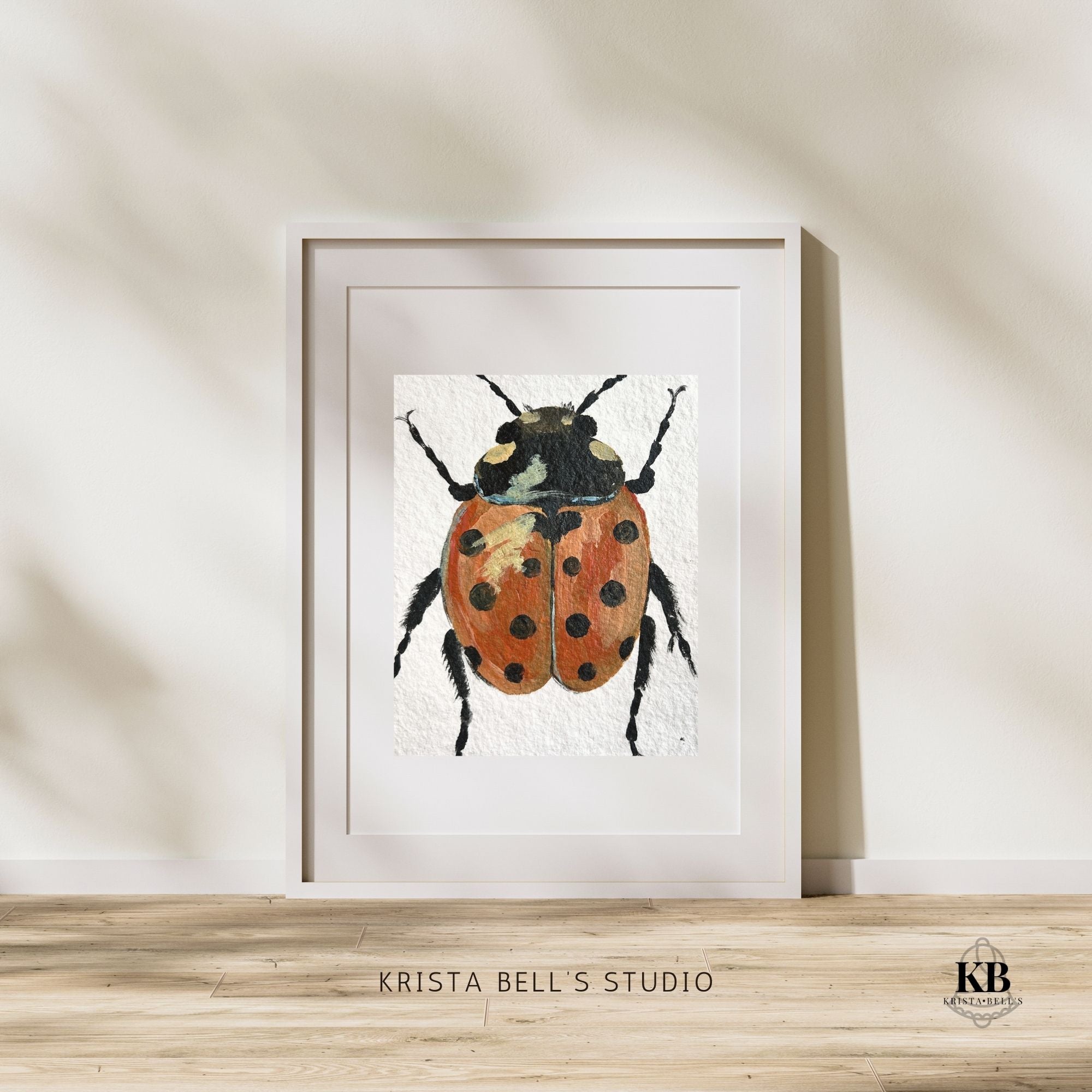 Framed artwork of a ladybug by Krista Bell's Studio on a wooden surface with a neutral background.