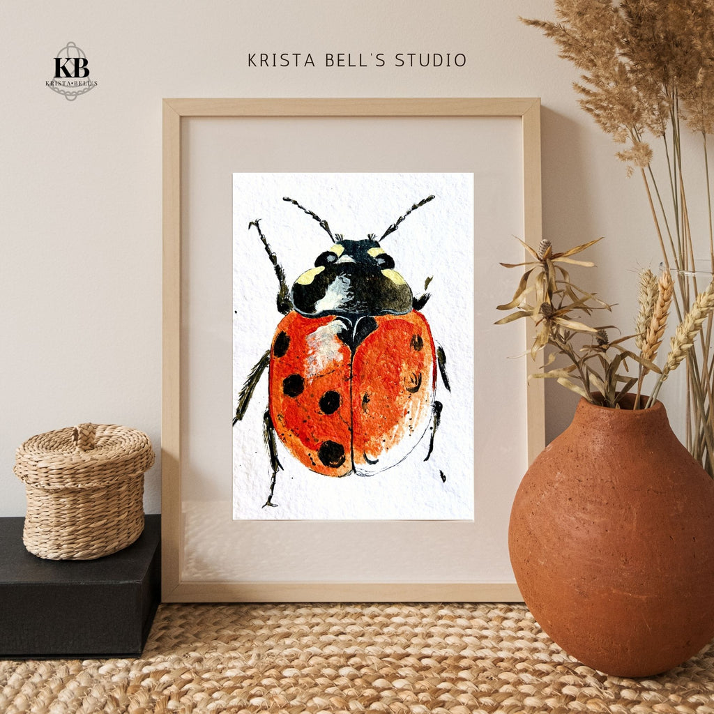 Framed artwork of a ladybug by Krista Bell's Studio on a neutral wall with decorative elements.
