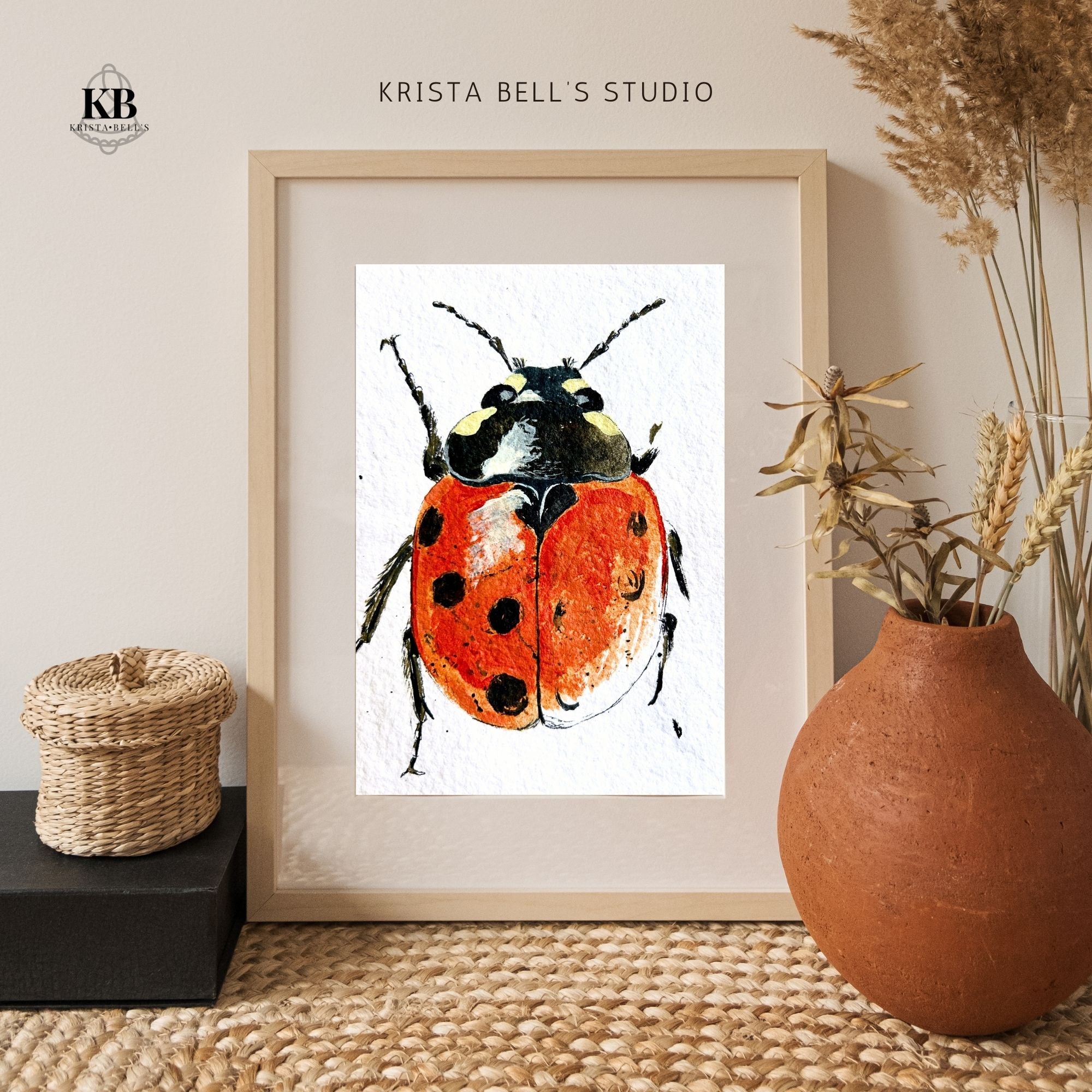 Framed artwork of a ladybug by Krista Bell's Studio on a neutral wall with decorative elements.