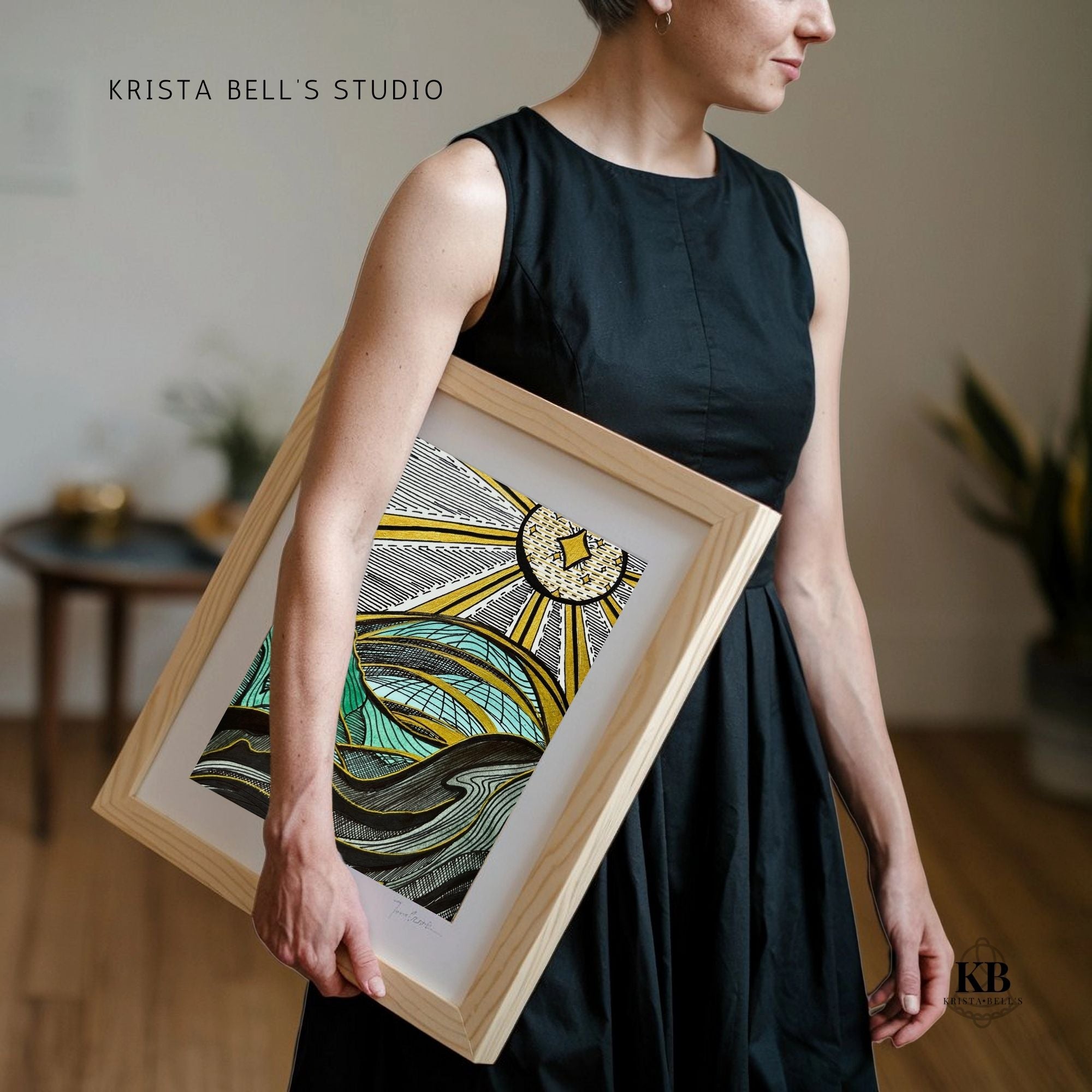 Woman holding a framed piece of art in a home setting with 'Krista Bell's Studio' branding.