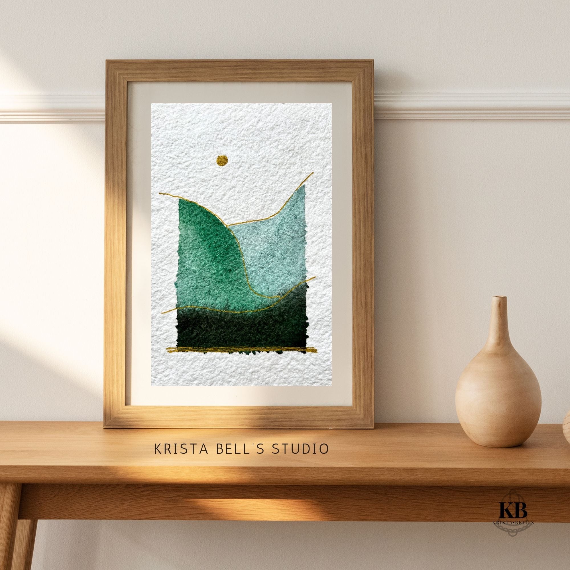 Framed artwork by Krista Bell's Studio on a wooden shelf with a neutral background. Simple modern watercolor landscape