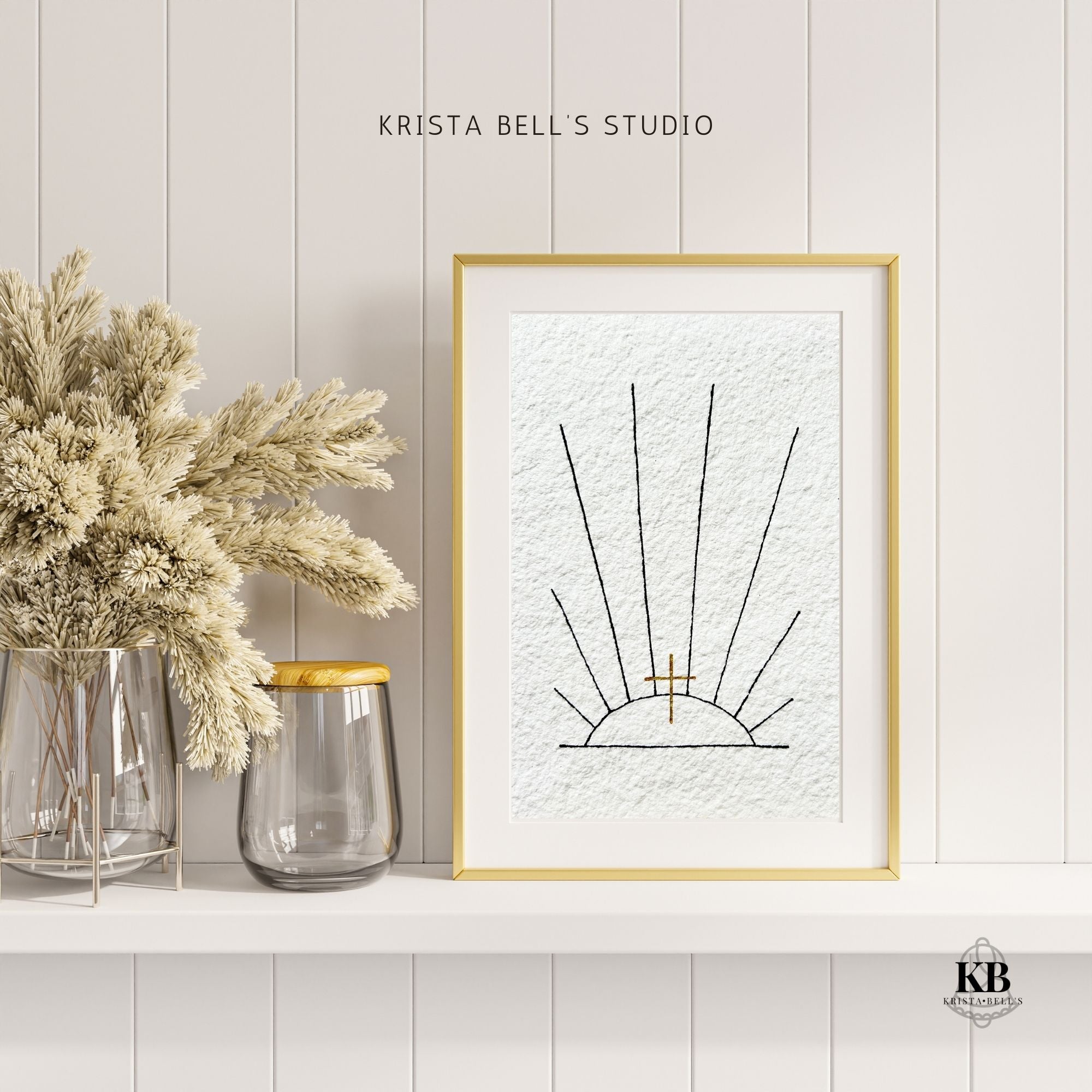 Framed artwork of black ink sunrays and a golden cross on a wall with decorative jars and dried plants.