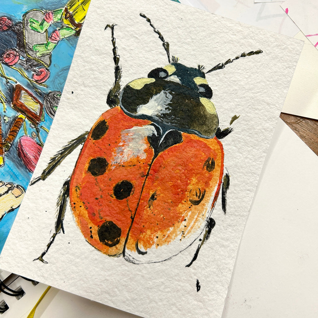 Painting of a ladybug on textured paper with other artworks in the background