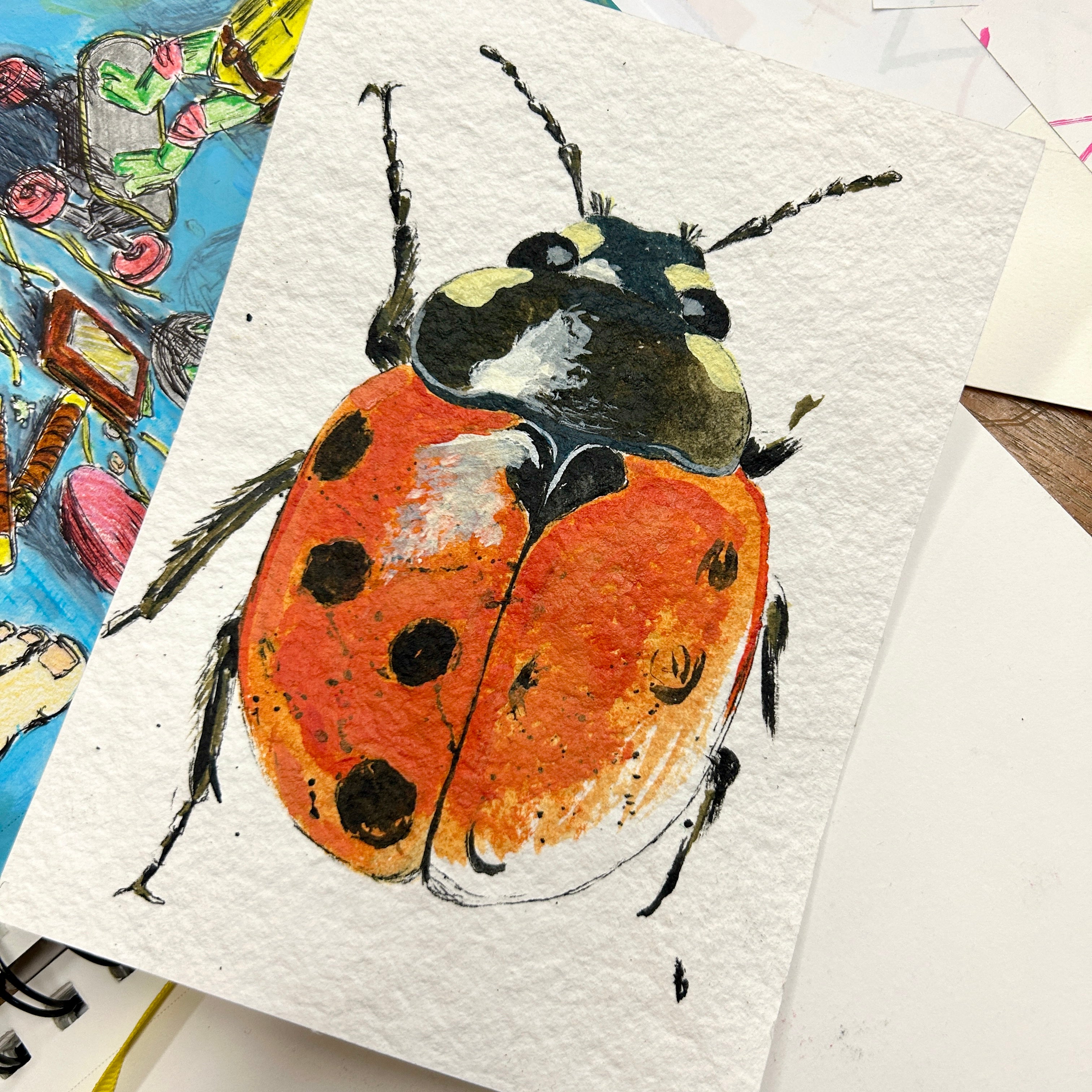 Painting of a ladybug on textured paper with other artworks in the background