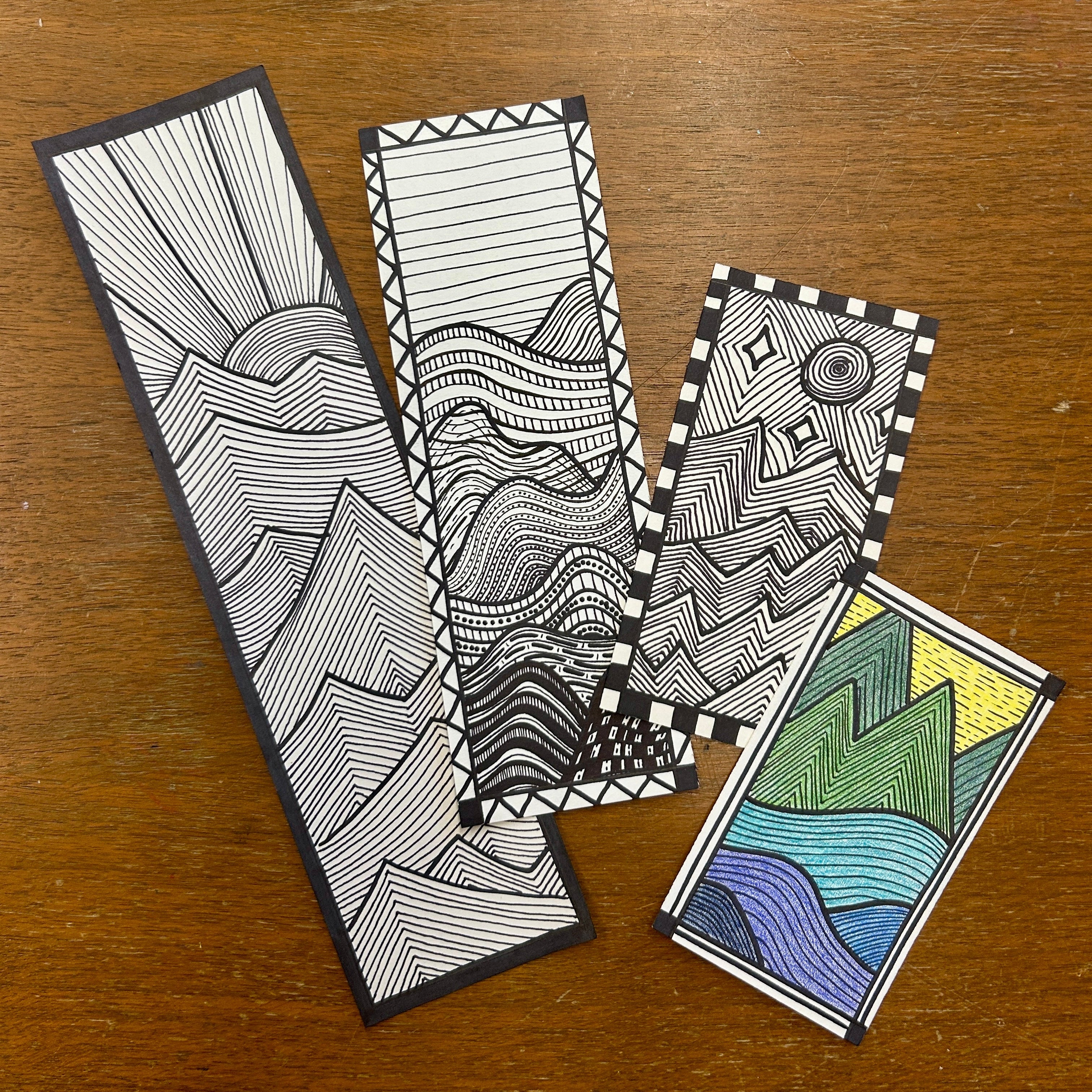 Four zentangle bookmarks on a wooden surface. Each depicting a modern geometric landscape ink drawing.