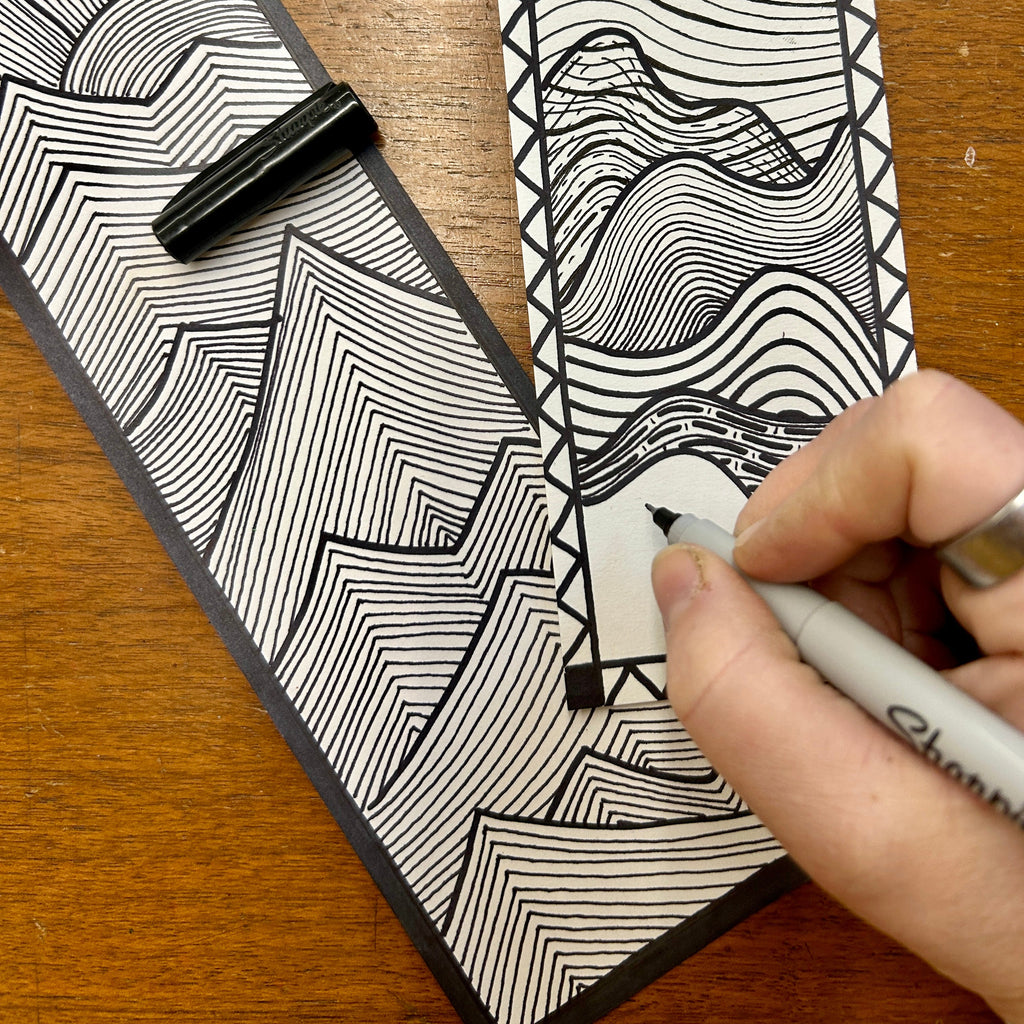 Person drawing a black and white line art design on a piece of paper with a pen.