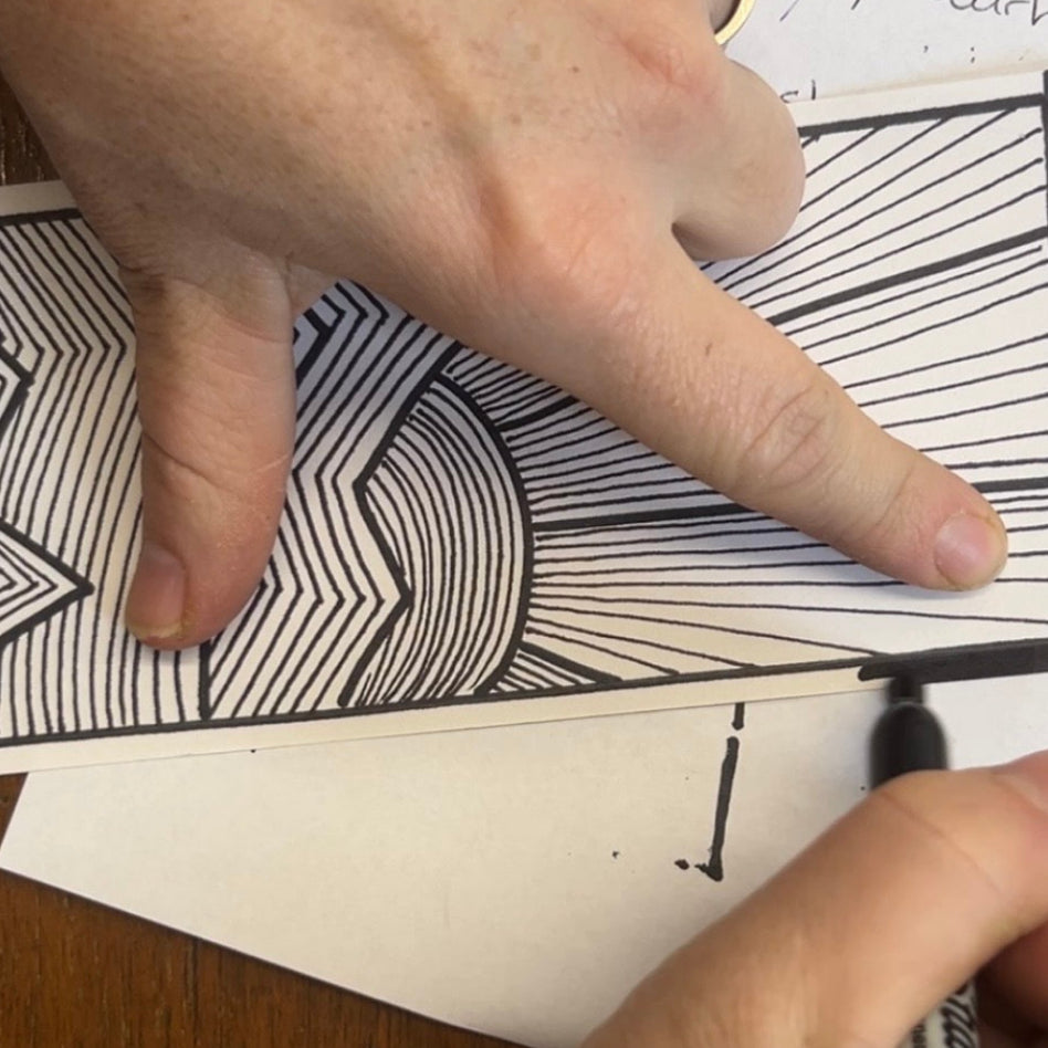Person drawing a geometric pattern with permanent black ink on white paper.
