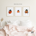 Three framed illustrations of ladybugs above a bed with pink bedding, featuring 'Krista Bells Studio' branding.