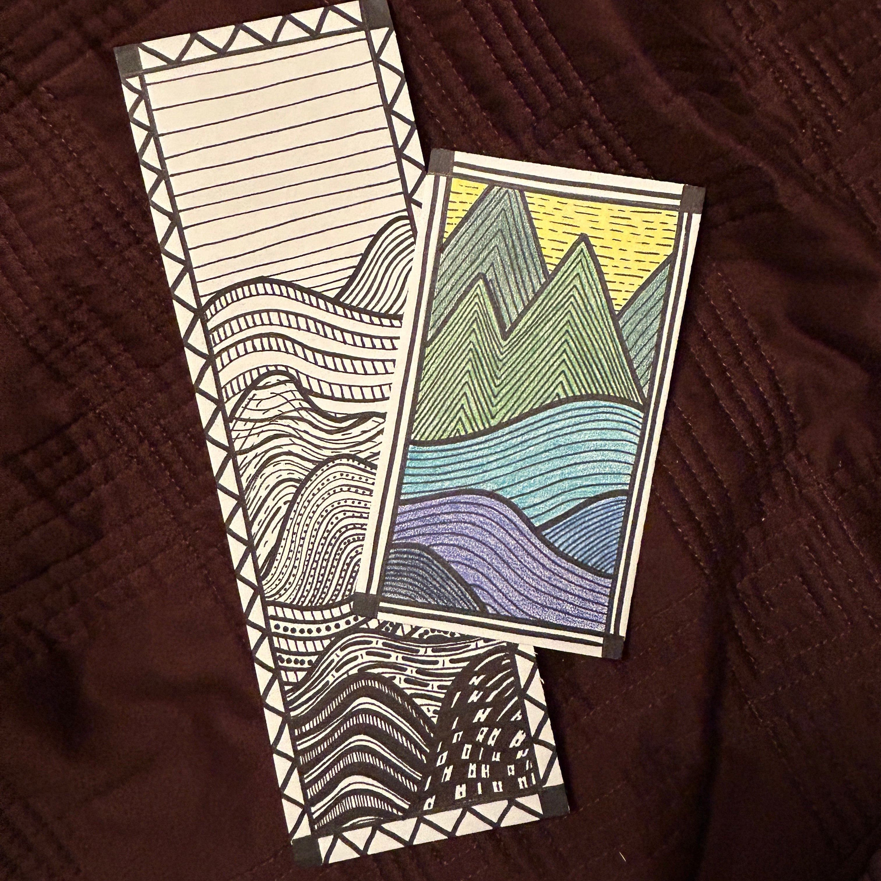 Two card designs with geometric line art landscape patterns on a brown textured surface.